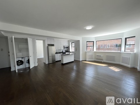 A spacious room with wooden floors and a kitchen area with white appliances.