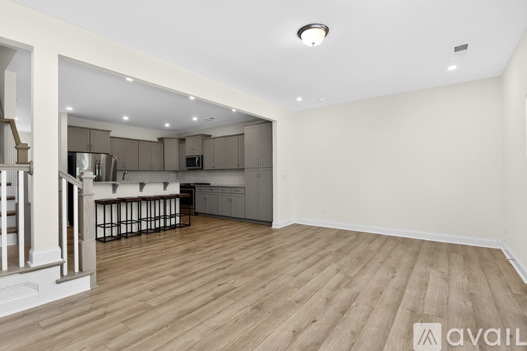 A spacious room with wooden flooring and a staircase in the background.