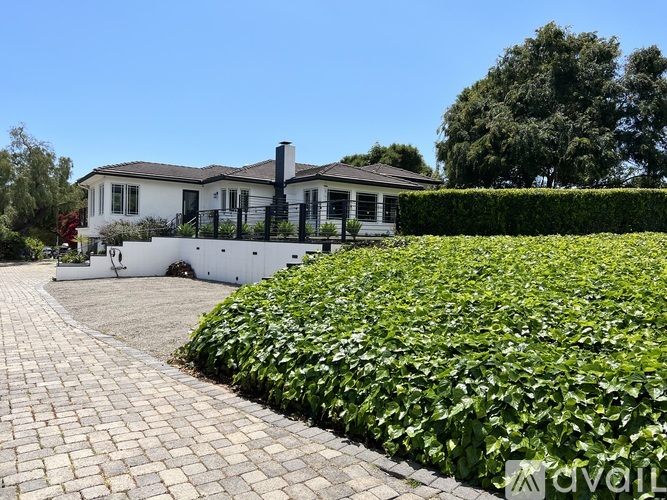 A house with a white exterior and a black fence is surrounded by a green hedge.