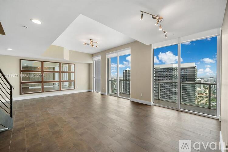 A spacious living room with hardwood floors and large windows overlooking a cityscape.