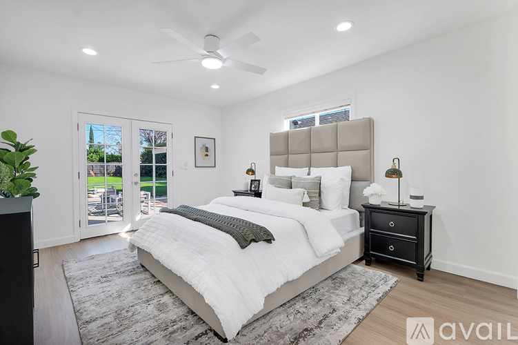A bedroom with a large bed, a ceiling fan, and a view of the backyard through a sliding glass door.