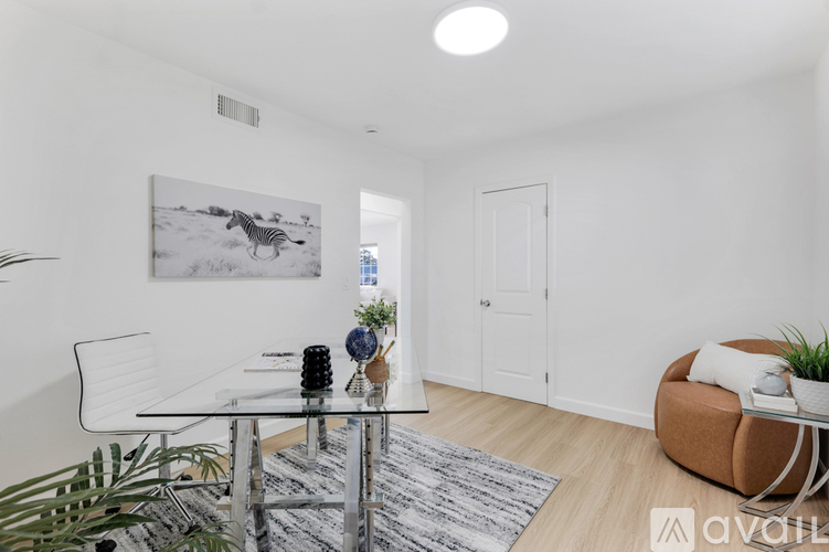 A modern dining room with a glass table and chairs, a framed picture of a zebra on the wall, and a carpeted floor.