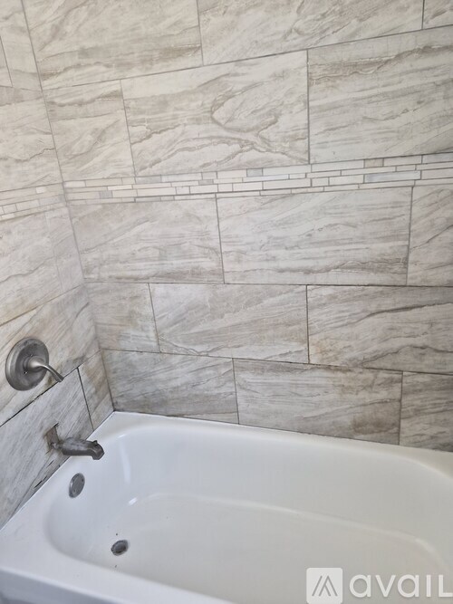 A white bathtub with a silver faucet is in a bathroom with a tiled wall.