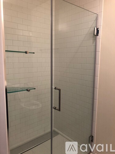 A glass shower door with a glass shelf and a white tiled wall.