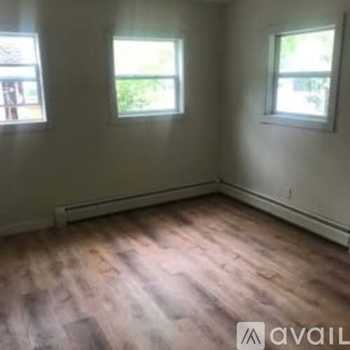 A room with wooden flooring and two windows.