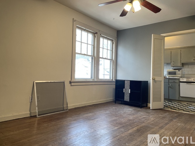 A room with a fan, a window, and a door leading to a kitchen.