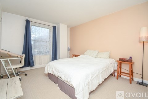 A bedroom with a white bed and a window with blue curtains.