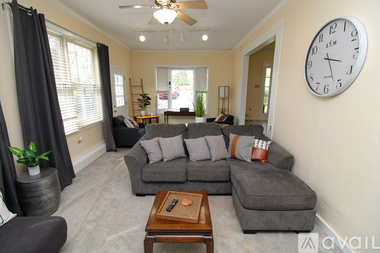 A living room with a grey couch, a wooden coffee table, and a large clock on the wall.