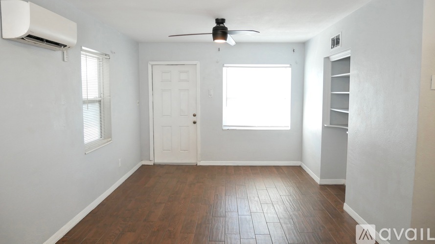 A room with a white door, a window with blinds, a ceiling fan, and a wall-mounted air conditioner unit.