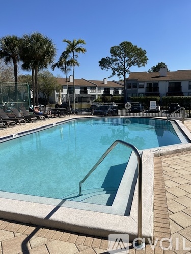 A pool surrounded by palm trees and a building in the background.