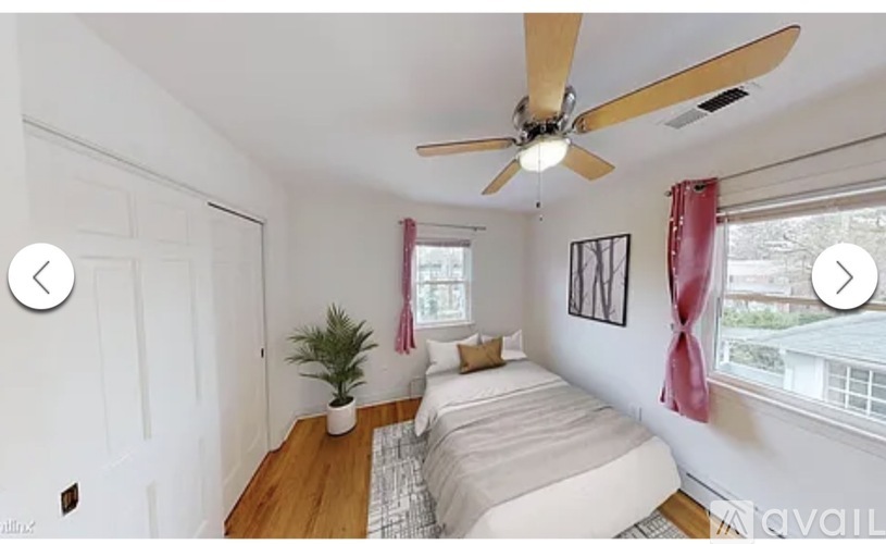 A bedroom with a bed, a ceiling fan, and a window with red curtains.