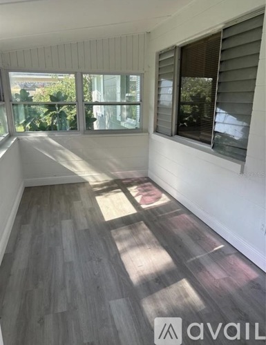 A room with white walls and wooden flooring with sunlight coming through the windows.