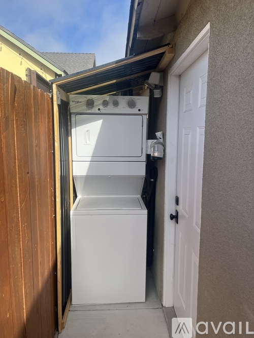 A white dishwasher is installed in a narrow space between a wooden fence and a house wall.