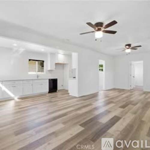 A spacious room with wooden flooring and two ceiling fans.