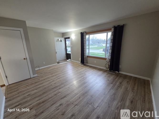 A room with wooden flooring and a window overlooking a green area.