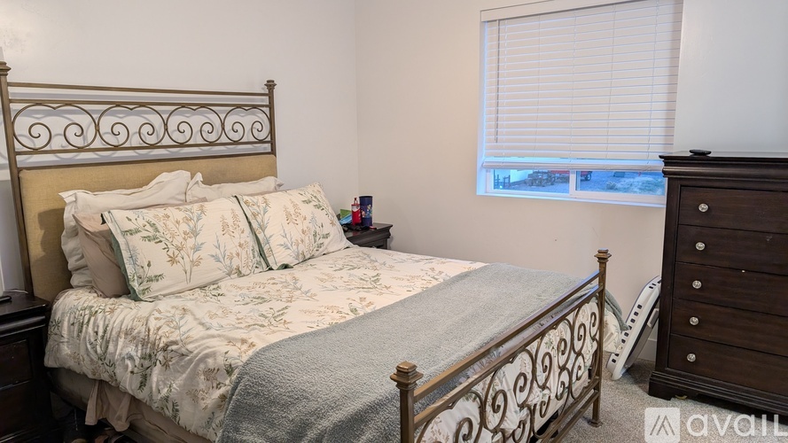 A bedroom with a bed, nightstand, and window with blinds.