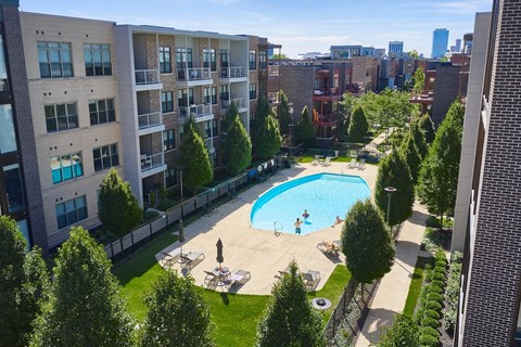 A swimming pool surrounded by trees and people relaxing in the sun.