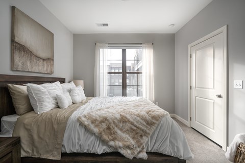 A bedroom with a bed covered in a tan and white comforter.