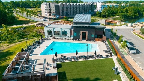 A large swimming pool is surrounded by a grassy area and a building with a red roof.