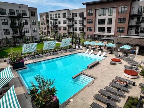 A swimming pool surrounded by lounge chairs and umbrellas in a sunny outdoor setting.