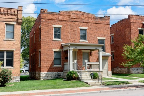 A red brick house with a white porch and a small front yard.