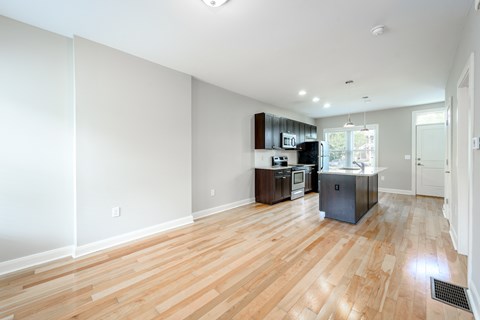 A kitchen with a sink, stove, and refrigerator in a room with wooden floors.