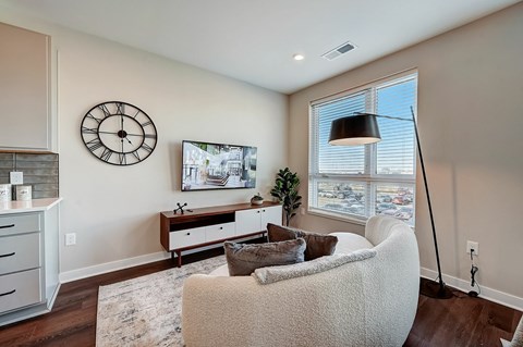 A living room with a white couch, a wooden cabinet, a clock, a plant, and a painting on the wall.