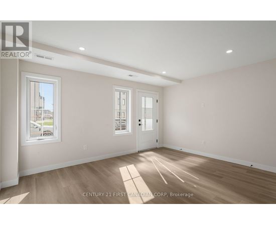 A spacious room with wooden flooring and two windows.