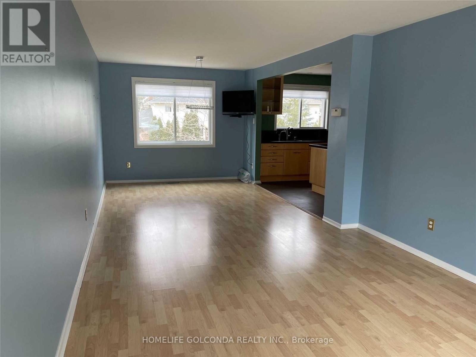 A room with wooden flooring and a window with a view of trees and a house.