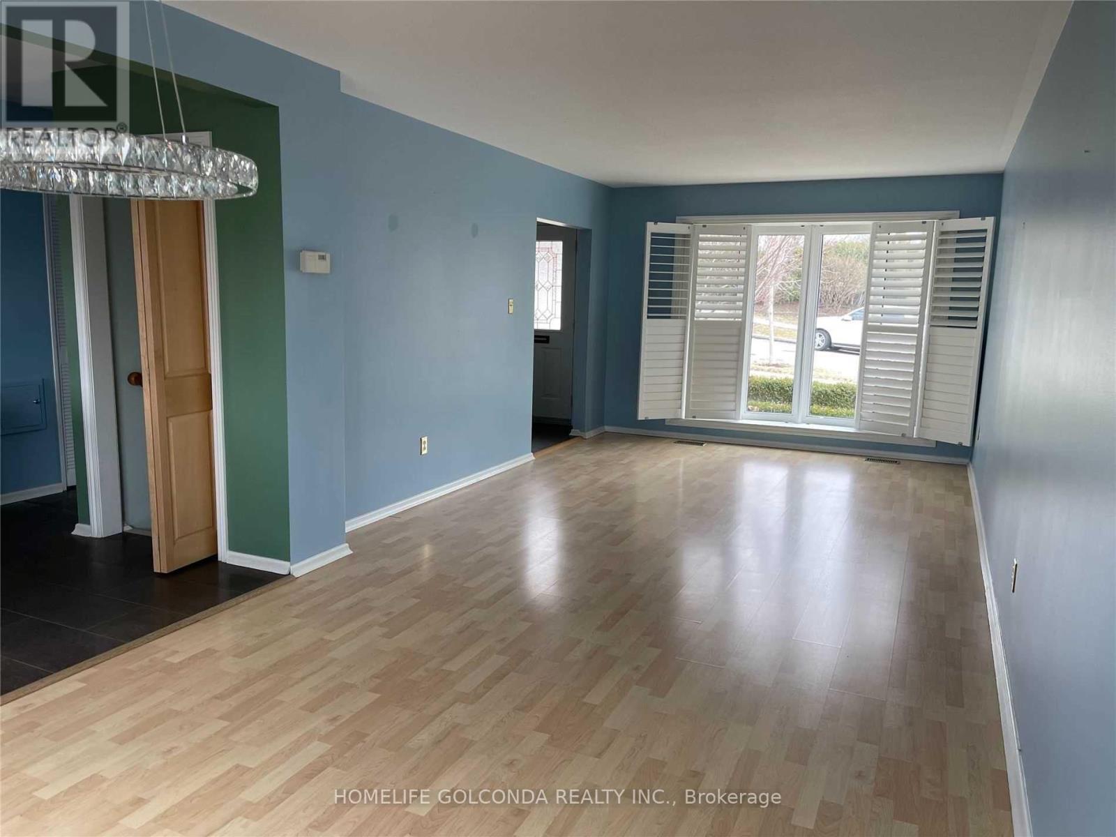 A room with wooden flooring and a large window with white blinds.