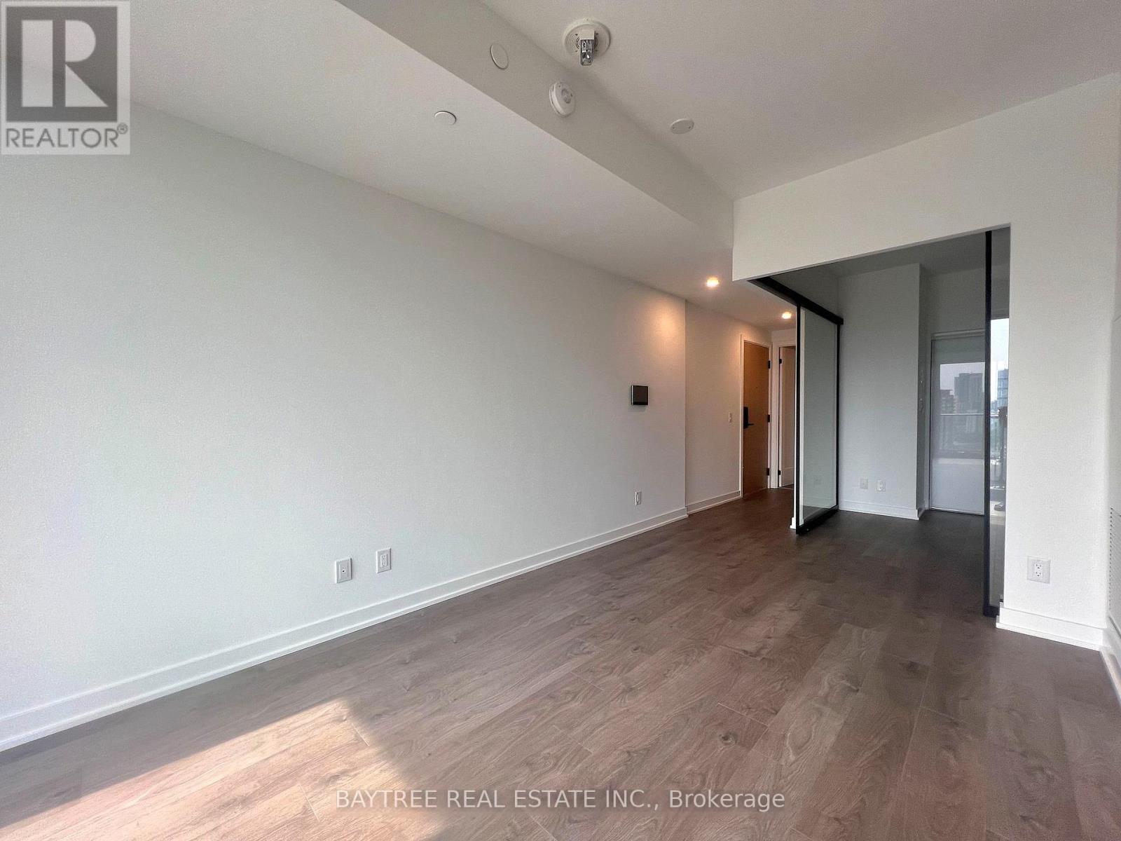 A spacious room with wooden flooring and white walls, part of a Baytree Real Estate Inc. property in Brokerage.