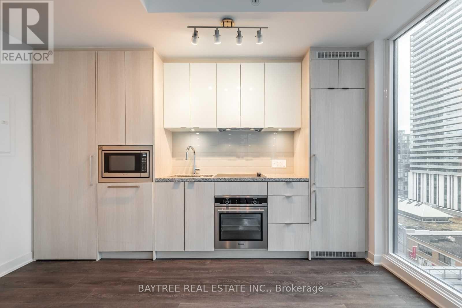 A modern kitchen with white cabinets and a large window.