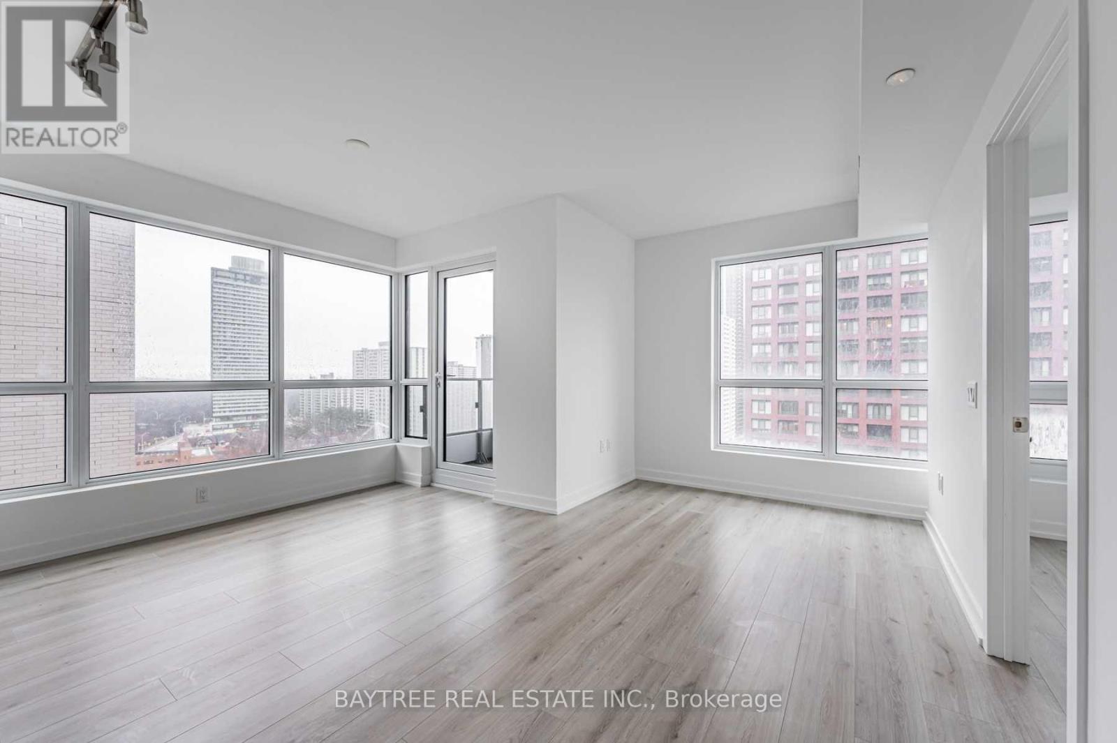 A spacious room with wooden floors and large windows overlooking a cityscape.