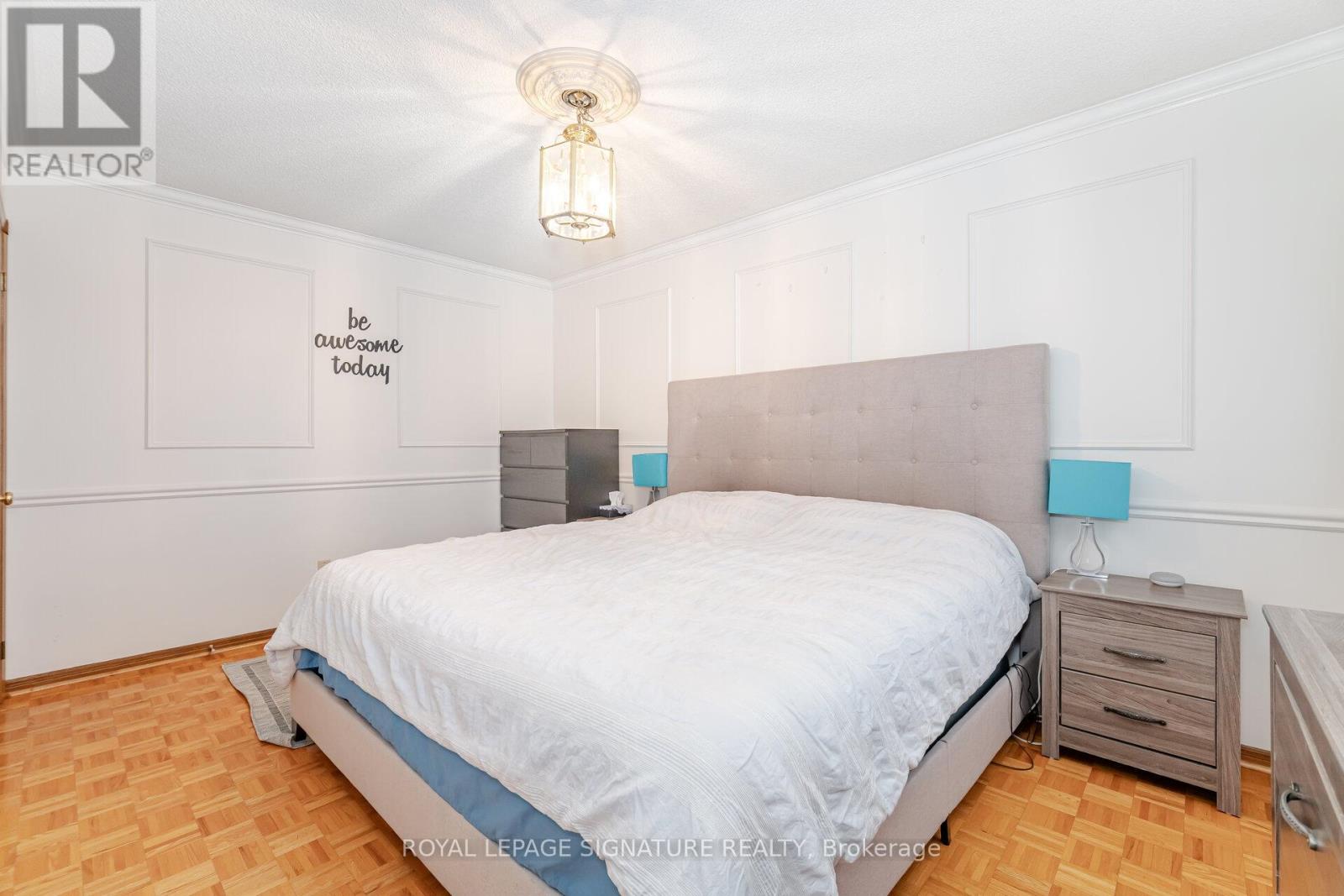 A bedroom with a bed, nightstand, and a wall with a "be awesome today" sign.
