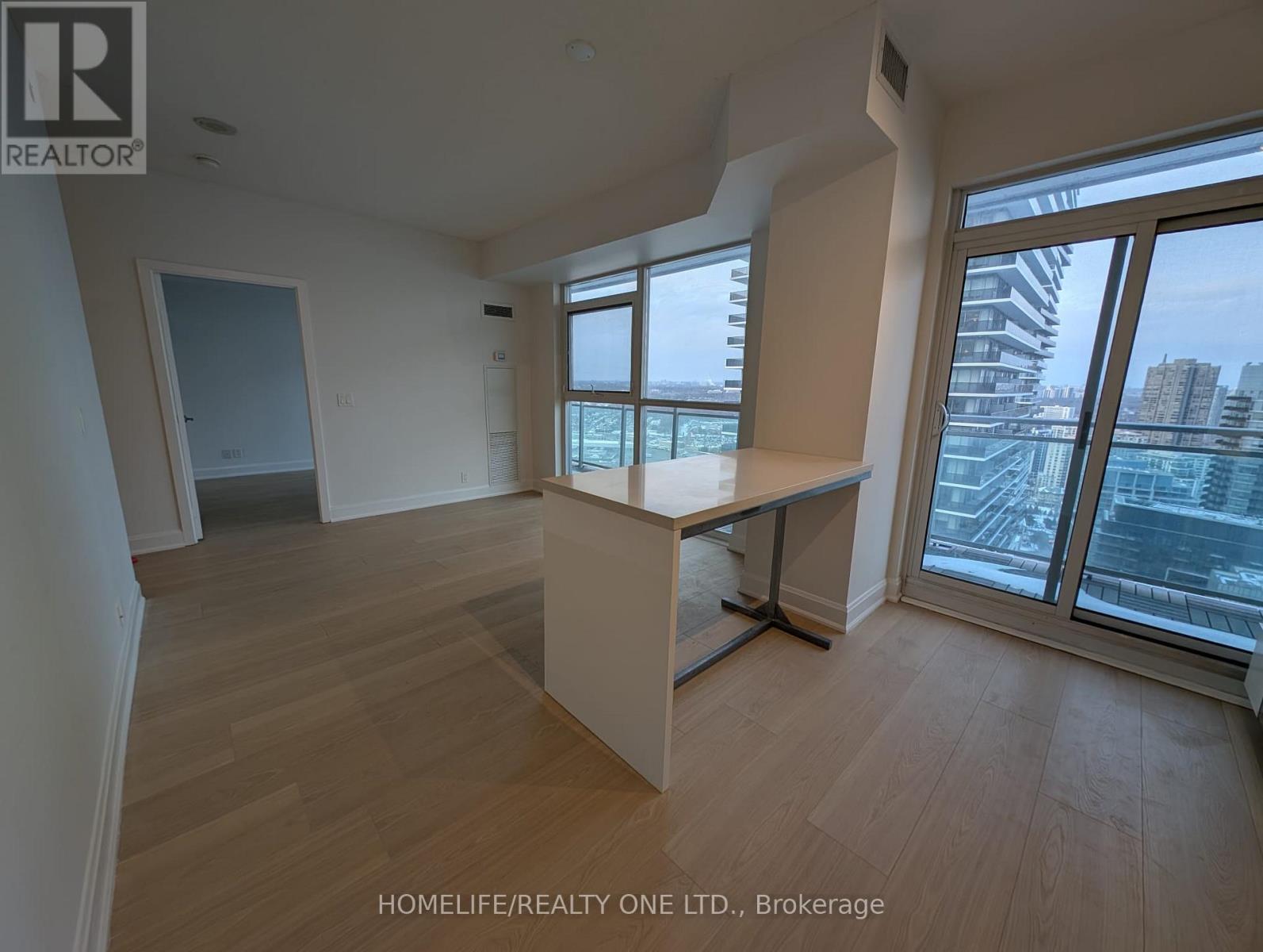 A spacious room with wooden flooring and large windows overlooking a cityscape.
