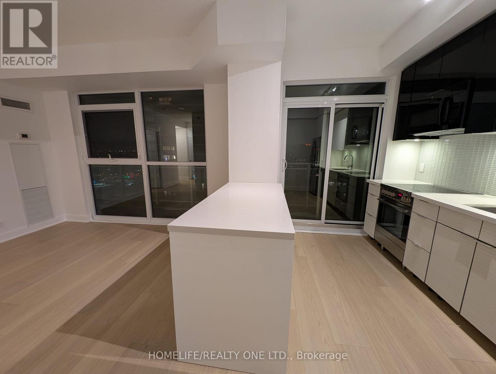 A modern kitchen with wooden flooring and white cabinetry.