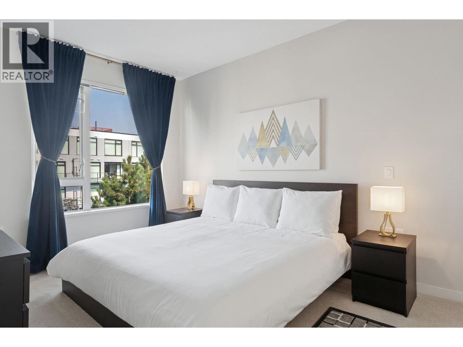 A bedroom with a large bed, a nightstand with a lamp, and a framed picture on the wall.