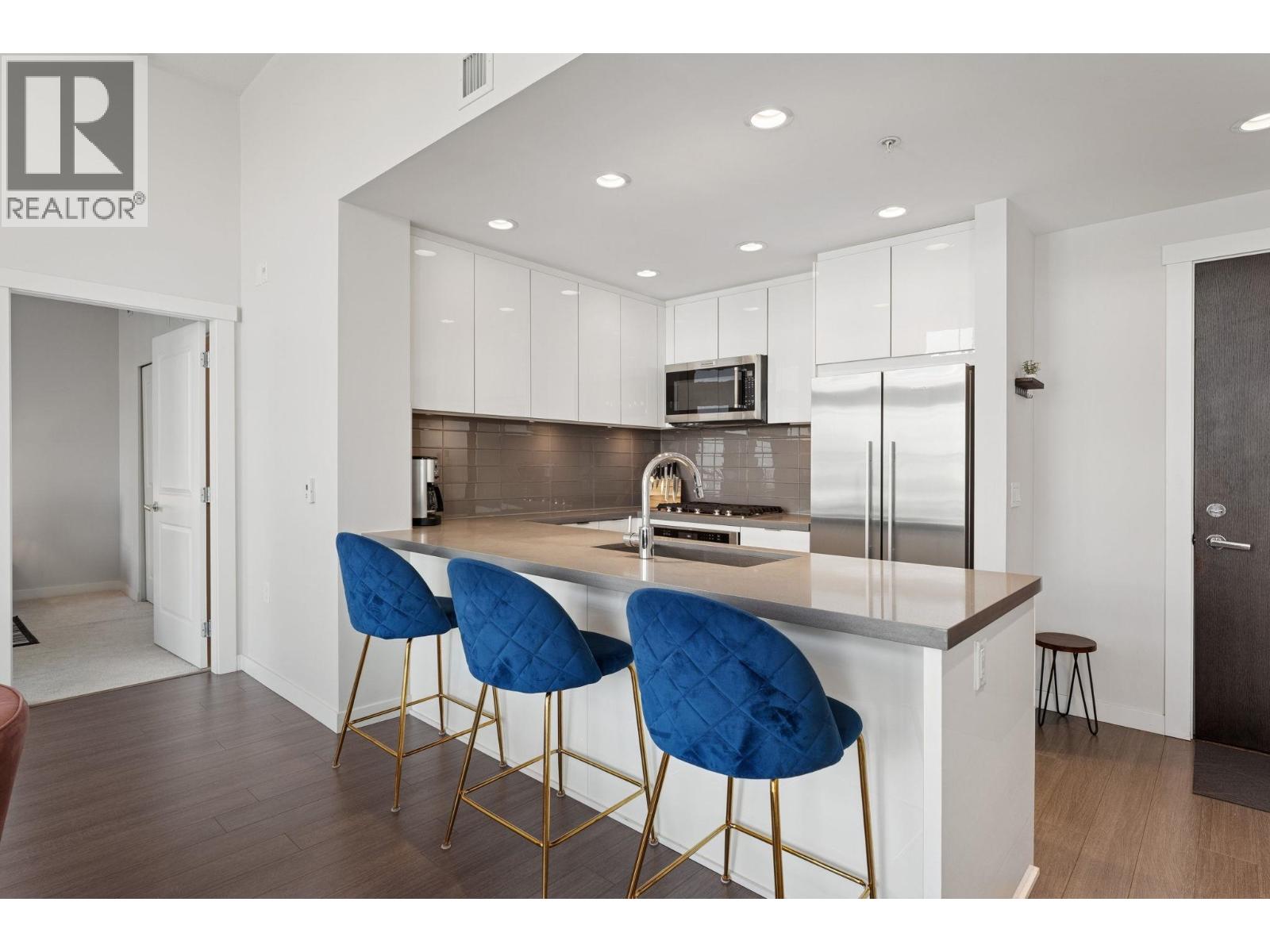 A modern kitchen with white cabinets and a bar area with blue chairs.