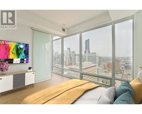 A modern bedroom with a large bed and a city view through the windows.