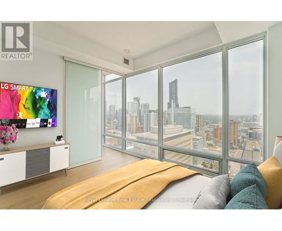 A modern bedroom with a large bed and a city view through the windows.