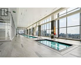 A large indoor swimming pool with a glass bottom is surrounded by a spacious, well-lit room with large windows.