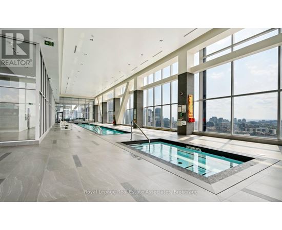 A large indoor swimming pool with a glass bottom is surrounded by a spacious, well-lit room with large windows.