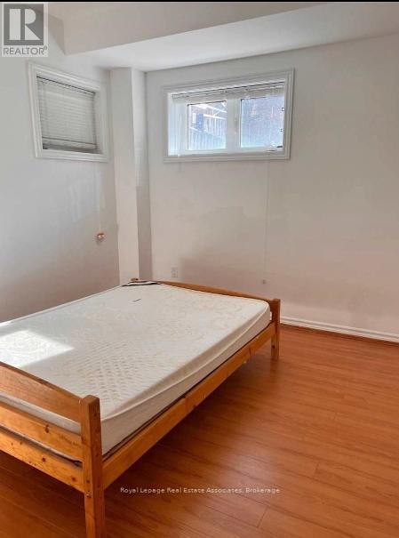 A bedroom with a bed, wooden floors, and two windows.