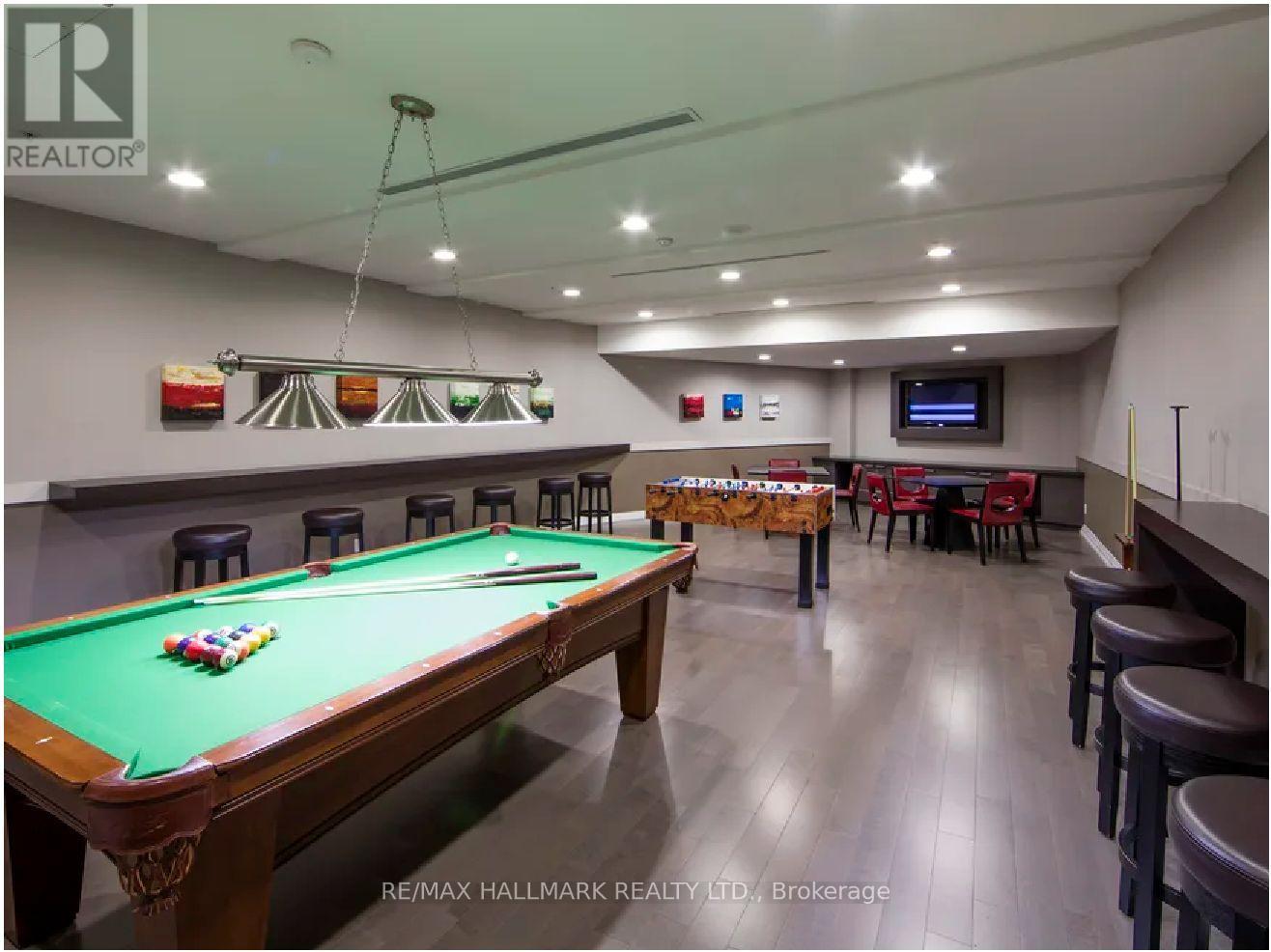 A pool table is in the middle of a room with a bar and a TV.