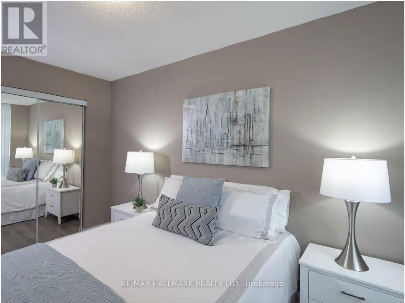 A bedroom with a large bed, two nightstands with lamps, and a painting on the wall.