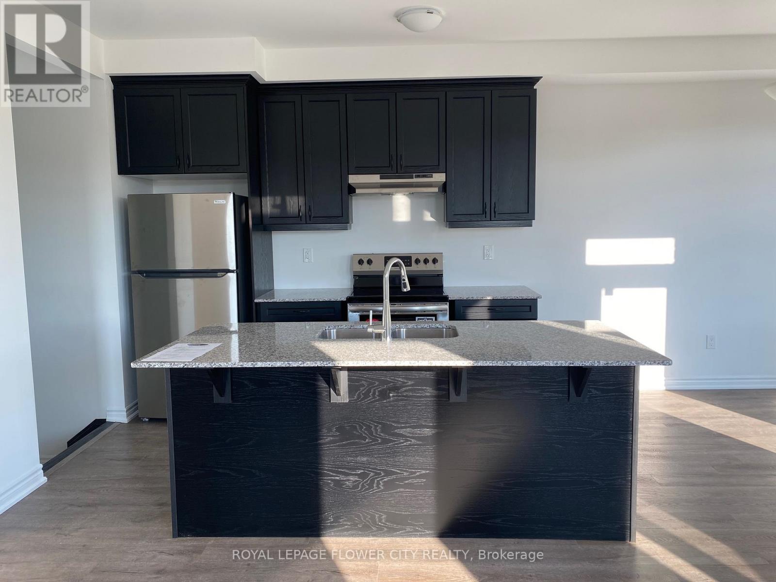 A kitchen with black cabinets and a stainless steel refrigerator.