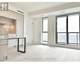 A spacious, empty room with a kitchen area to the left and a large window with a view of the city.