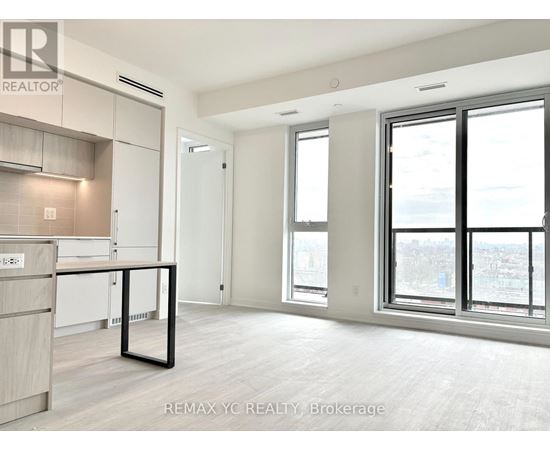 A spacious, empty room with a kitchen area to the left and a large window with a view of the city.
