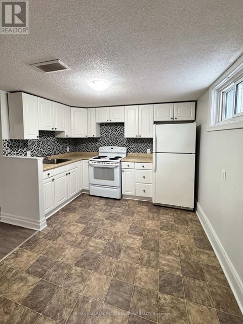A kitchen with white appliances and brown tiled flooring.