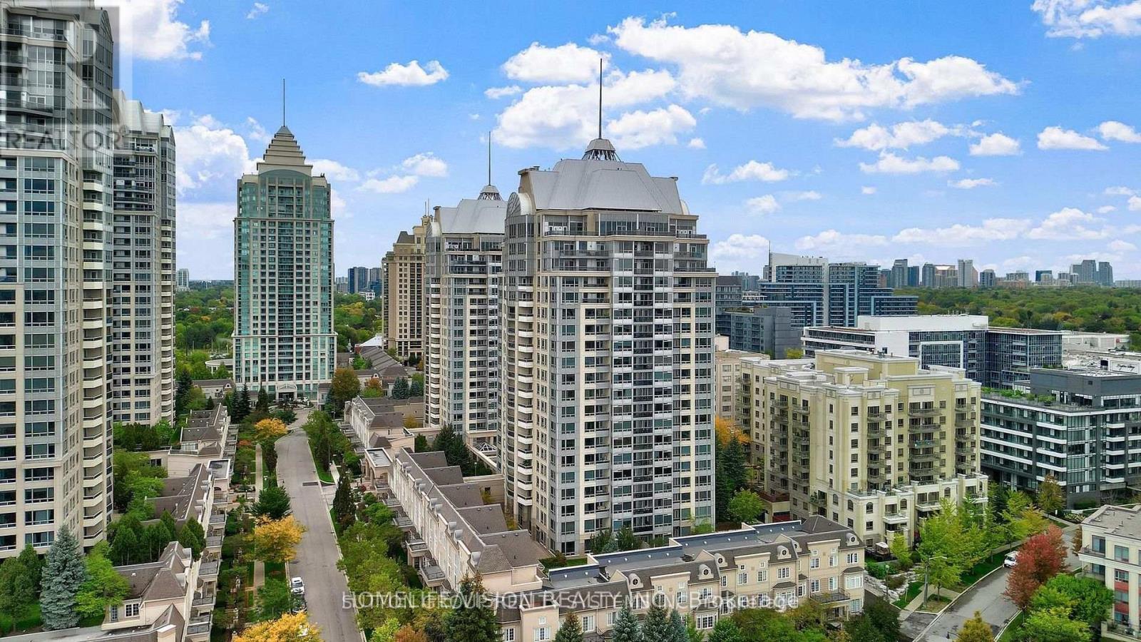A cityscape with a mix of modern and older buildings, a clear sky, and a road with trees on the side.